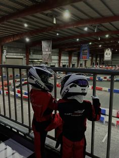 two young children wearing helmets looking out over an obstacle course at the same time as they stand on a railing