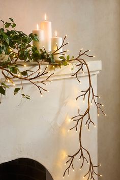 a white fireplace with candles and branches on it