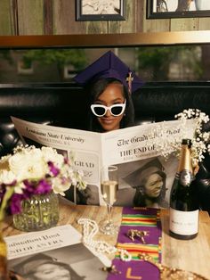 a woman sitting at a table in front of a book and wine bottle with glasses on it