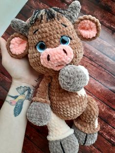 a hand holding a small stuffed animal in it's left arm, on top of a wooden table