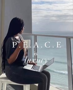 a woman sitting on top of a white chair next to a window looking out at the ocean