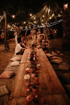 a group of people sitting around a long wooden table with lights strung over the top