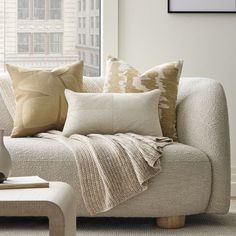 a white couch with pillows on it in front of a window and a table next to it