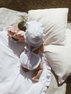 a little baby sitting on top of a white blanket next to pillows and pink flowers