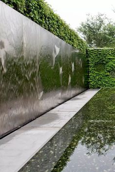 an outdoor pool with water running down the side and greenery on the wall behind it