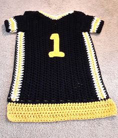 a crocheted black and yellow shirt with the number one on it sitting on carpet