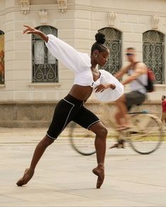 a woman is dancing on the street while people ride bikes behind her