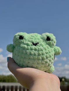 a hand holding a green crocheted stuffed animal with eyes on it's face