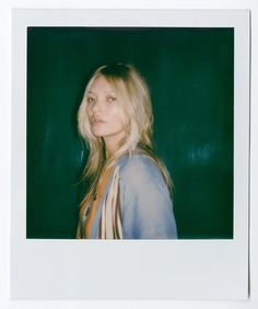 a polaroid photograph of a woman with long blonde hair and blue shirt, standing in front of a green background