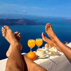 two people with their feet up on a ledge overlooking the ocean and orange juices