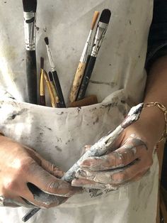 a person with paint on their hands and some brushes in the other hand while they are holding something