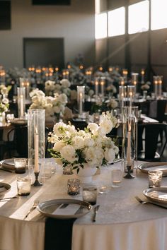 the table is set with silverware and white flowers in vases, candles and plates