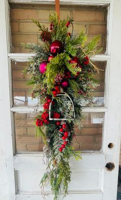 a wreath hanging on the front door of a house decorated with greenery and ornaments