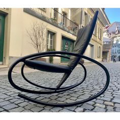 a black rocking chair sitting on top of a cobblestone road next to a building