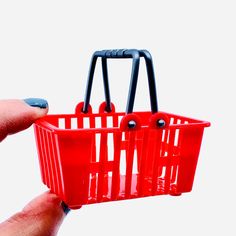 a hand holding a red shopping basket with black handles