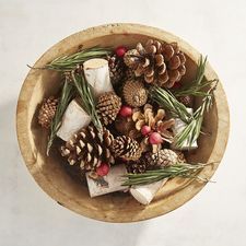 a wooden bowl filled with pine cones and other decorations on top of a white table