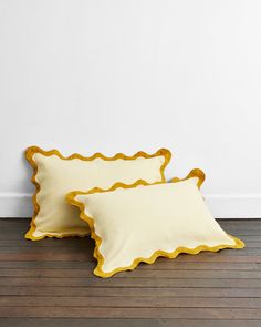 two yellow scalloped pillows sitting on top of a wooden floor next to a white wall