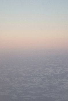 the view from an airplane looking down on some clouds and land in the distance at sunset