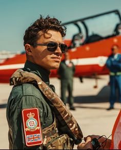 a man standing in front of an airplane with other people around him and wearing sunglasses