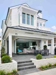 a white house with steps leading up to the front door and covered patio area, surrounded by greenery