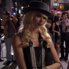 a woman with long blonde hair wearing a hat and pearls