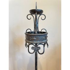 an ornate iron plant stand with two pots on it's sides and a candle holder in the middle