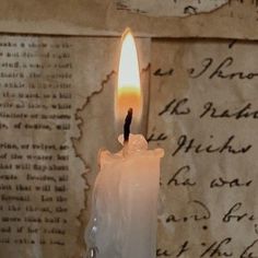 a lit candle sitting on top of a table next to a piece of old paper