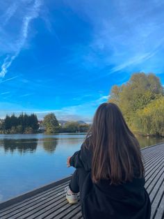 a woman sitting on a bench looking at the water and clouds in the sky above her