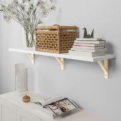 a shelf with books and baskets on it in a room next to a vase filled with baby's breath flowers