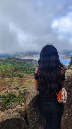 a woman sitting on top of a large rock next to a lush green valley and ocean