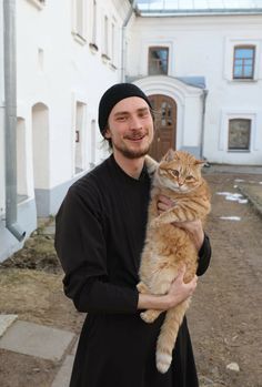 a man holding a cat in front of a white building and smiling at the camera