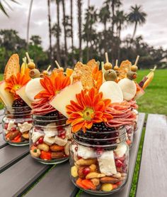 three jars filled with food sitting on top of a wooden table next to palm trees