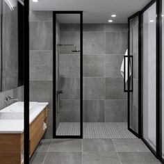 a bathroom with grey tiles and wooden cabinets, along with a walk - in shower