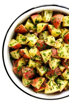 a white bowl filled with potatoes covered in seasoning and garnished with parsley