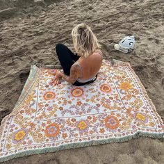 a woman sitting on top of a beach next to a colorful blanket with an orange and yellow flower pattern