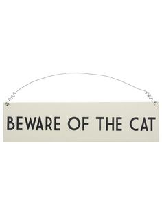 a sign that says beware of the cat hanging from a string on a white wall