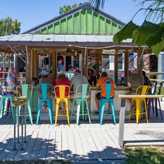 people sitting at tables in front of a building with colorful chairs and umbrellas on the deck