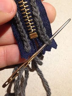 a person holding a pair of knitting needles in their left hand and the end of an open zipper