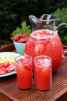 a pitcher of water with strawberries and lemons next to two glasses on a tray