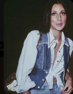 a woman with long hair wearing a denim vest and holding a handbag in her right hand