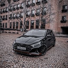 a black car parked in front of a tall building on a cobblestone street