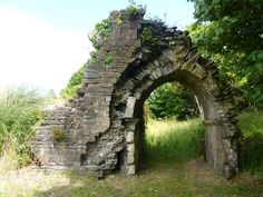 an old stone arch in the middle of a field with grass and trees around it