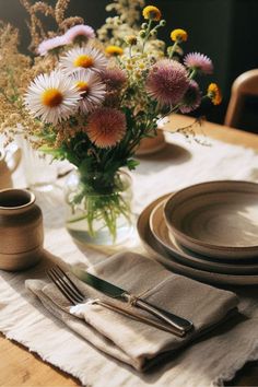 the table is set with flowers in a vase and place settings for two people to sit at