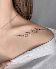 the back of a woman's shoulder with a branch tattoo on it