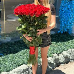 a woman holding a bunch of red roses in her hands and posing for the camera