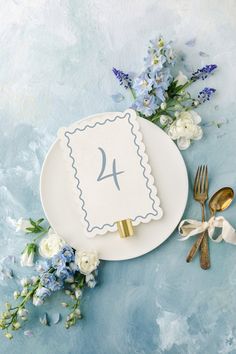 a white plate with a napkin and fork on it next to some blue flowers in the background