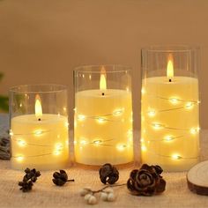 three lit candles sitting on top of a table next to some pine cones and nuts