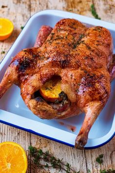 a whole chicken sitting on top of a white plate next to sliced oranges and herbs