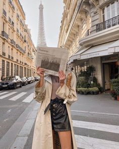 a woman standing in front of the eiffel tower holding up a newspaper to her face