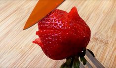 a strawberry being cut with a knife on a cutting board